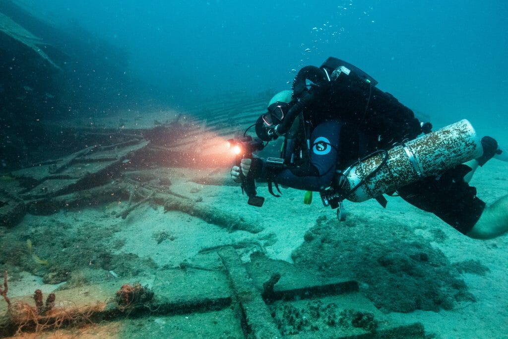 A diver underwater with a rebreather diving along a wreck