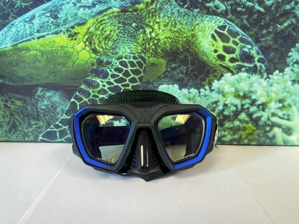 A prescription dive mask with custom lenses sits on a table in front of a photo of a sea turtle.