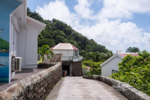 A scenic uphill road in Saba, lined with white houses and lush green hills in the background.
