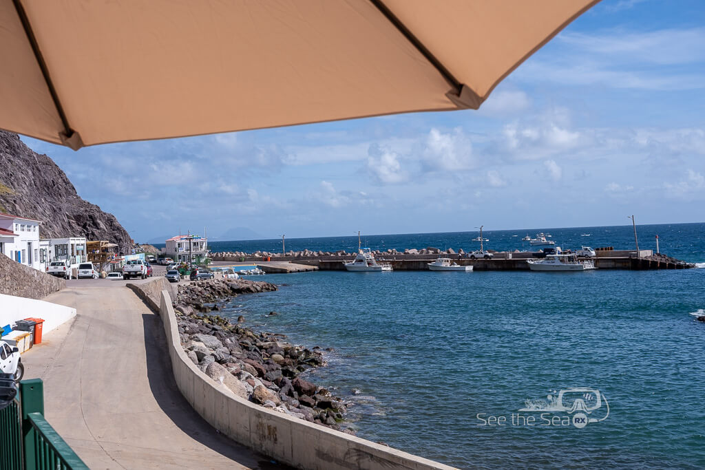A scenic seaside view in Saba, featuring a harbor with boats docked along the shoreline under a bright blue sky.