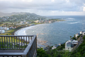 A scenic coastal view from a wooden balcony overlooking a bay with waves gently reaching the shore.